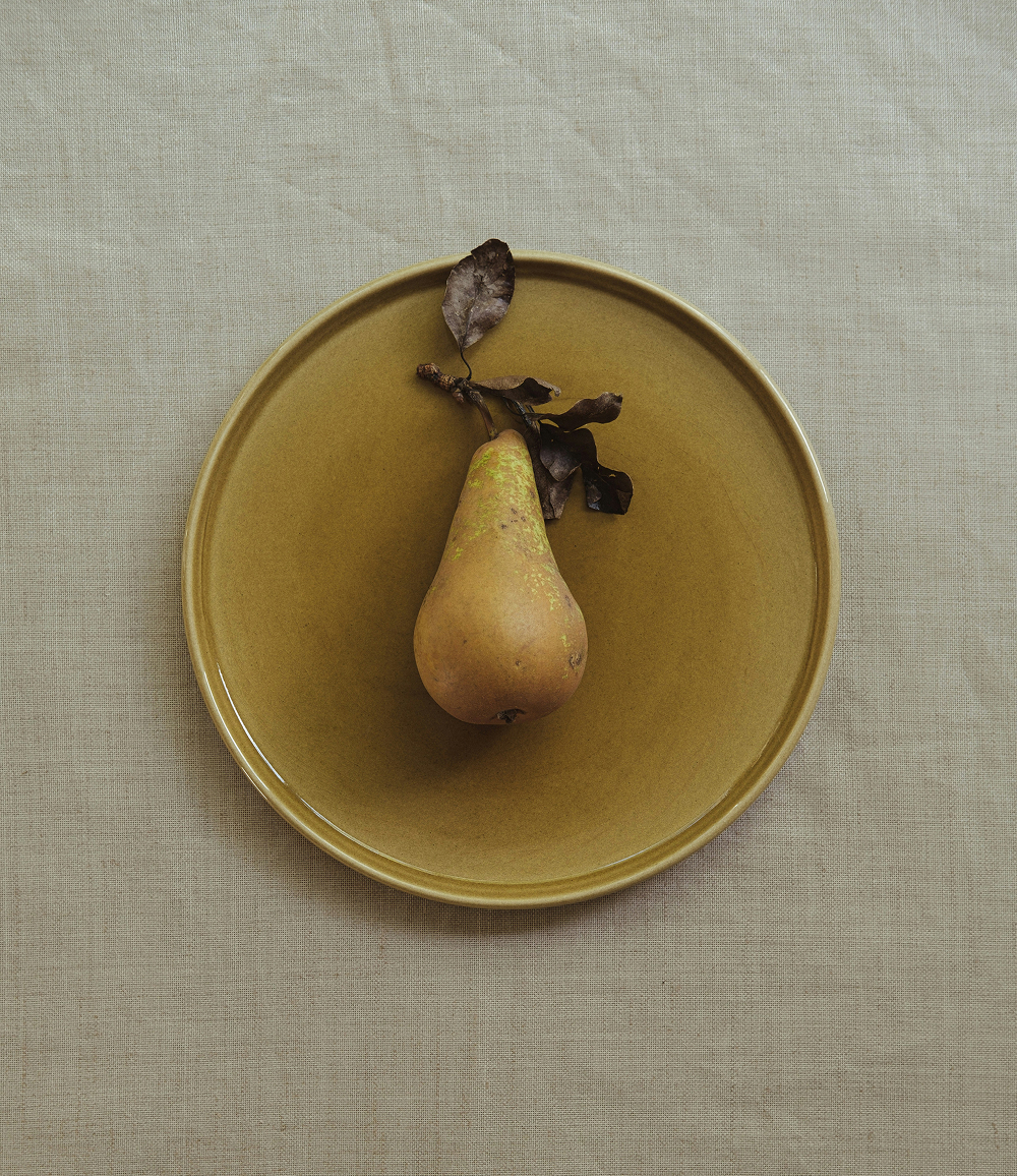 A pear set on a yellow plate upon a soft white canvas texture.